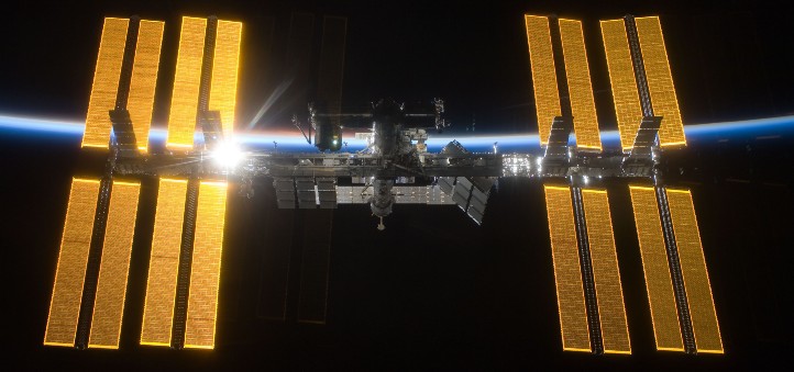 Die ISS im Licht der aufgehenden Sonne. Im Hintergrund sieht man die dünne Atmosphäre der Erde. Bild: NASA/ESA