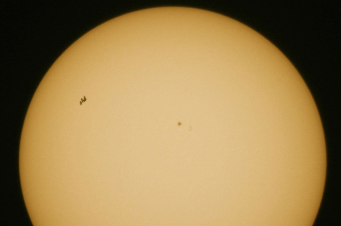 Eine ganz außergewöhnliche Aufnahme der ISS gelang DLR-Mitarbeiter Thilo Kranz. Er fotografierte die ISS gerade in dem Moment, als sie auf ihrer Bahn um die Erde – vom Boden aus gesehen – über die Sonne „huschte“. Das dauerte knapp eine Minute. Die ISS ist links oben zu sehen – in der Mitte sind kleine Sonnenflecken zu erkennen. 
Bild: Thilo Kranz (DLR)