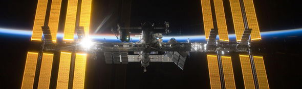 Auf diesem Bild sieht man die ISS vor der Nachtseite der Erde. Die aufgehende Sonne beleuchtet das dünne Band der Atmosphäre. Bild: NASA