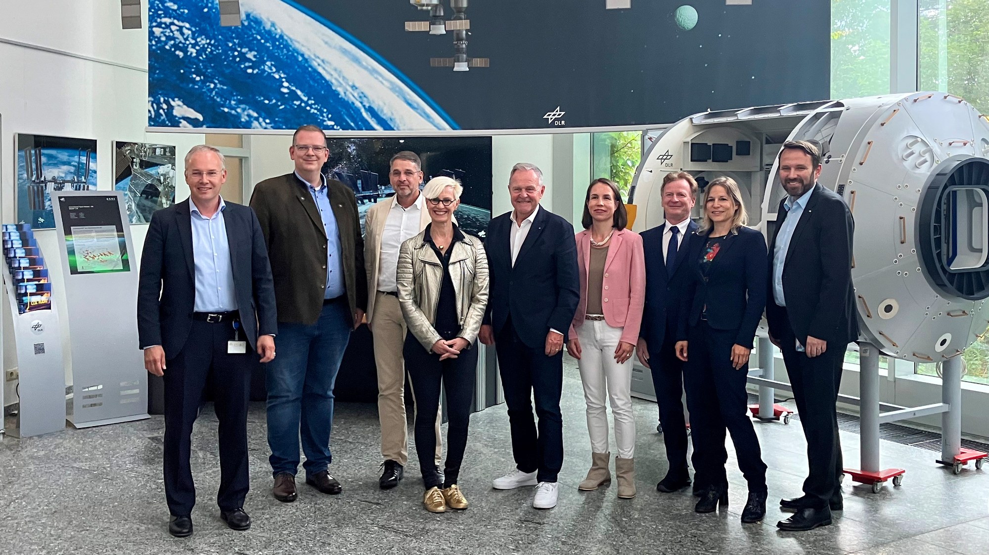 Gruppenfoto der Delegation vor dem kleinen Columbus-Modell im Raumfahrtkontrollzentrum in Oberpfaffenhofen