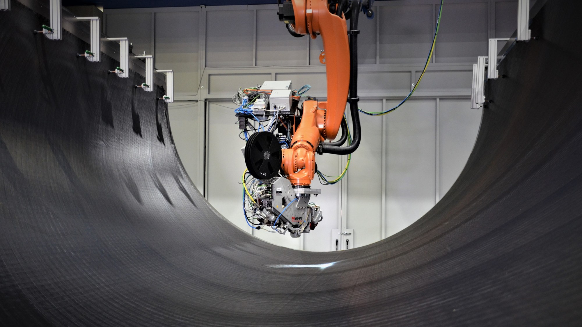 Ein orangener Roboterarm steht bereit zur in-situ Konsolidierung in der Werkzeug-Form der Flugzeughaut.