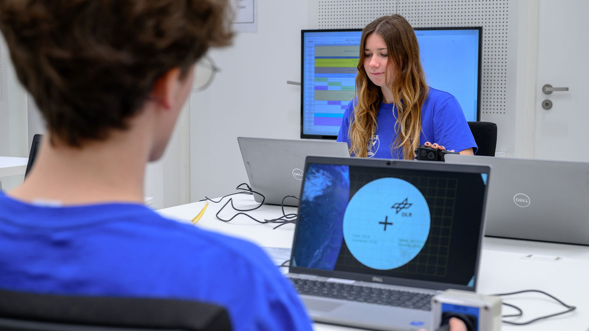 Eine junge Frau und ein junger Mann sitzen vor einem Bildschirm und versuchen, mit einem Joystick das virtuelle Raumschiff zu positionieren.