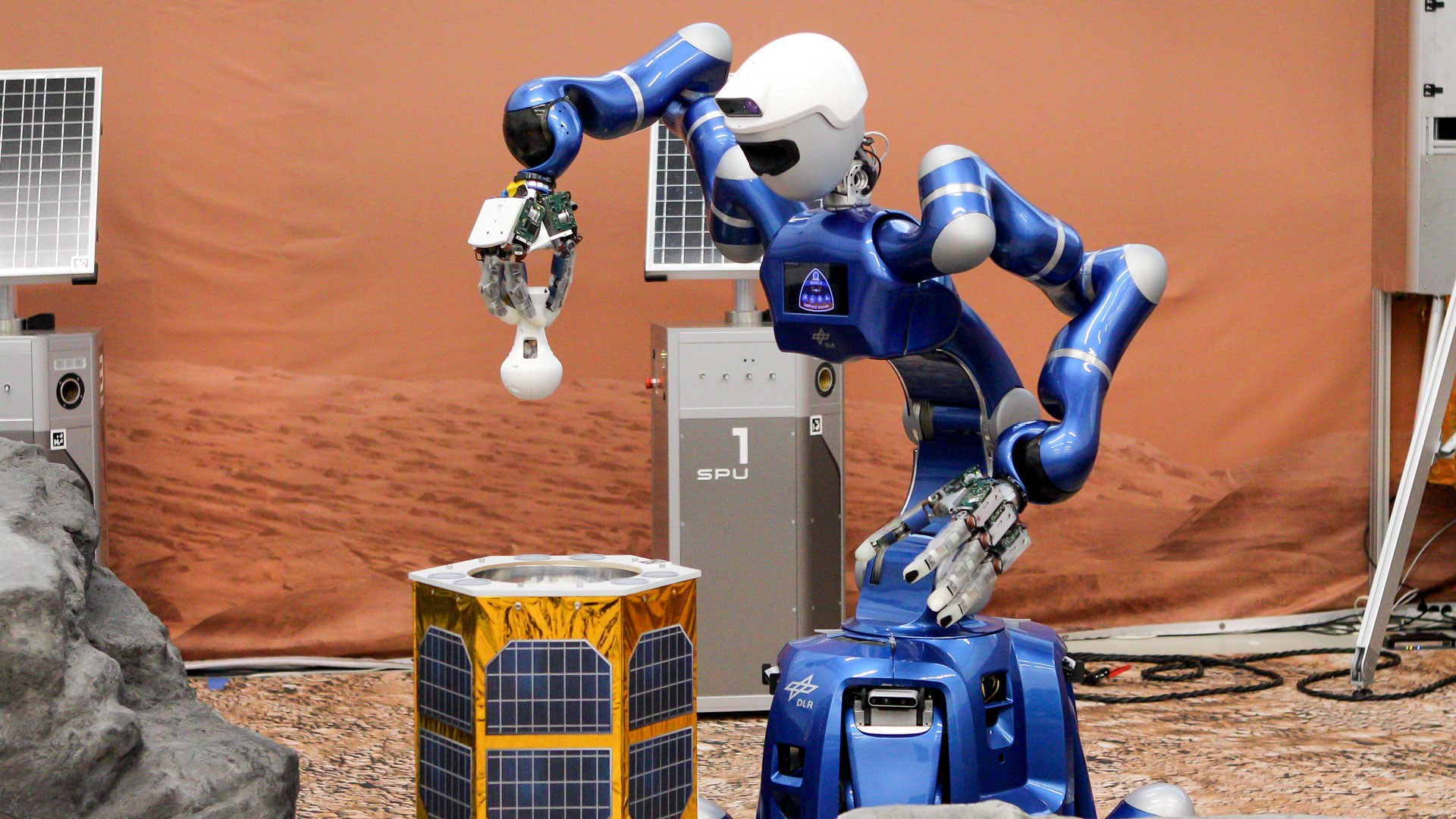 Ein blauer, humanoider Roboter hält einen Probenbehälter in der Hand.