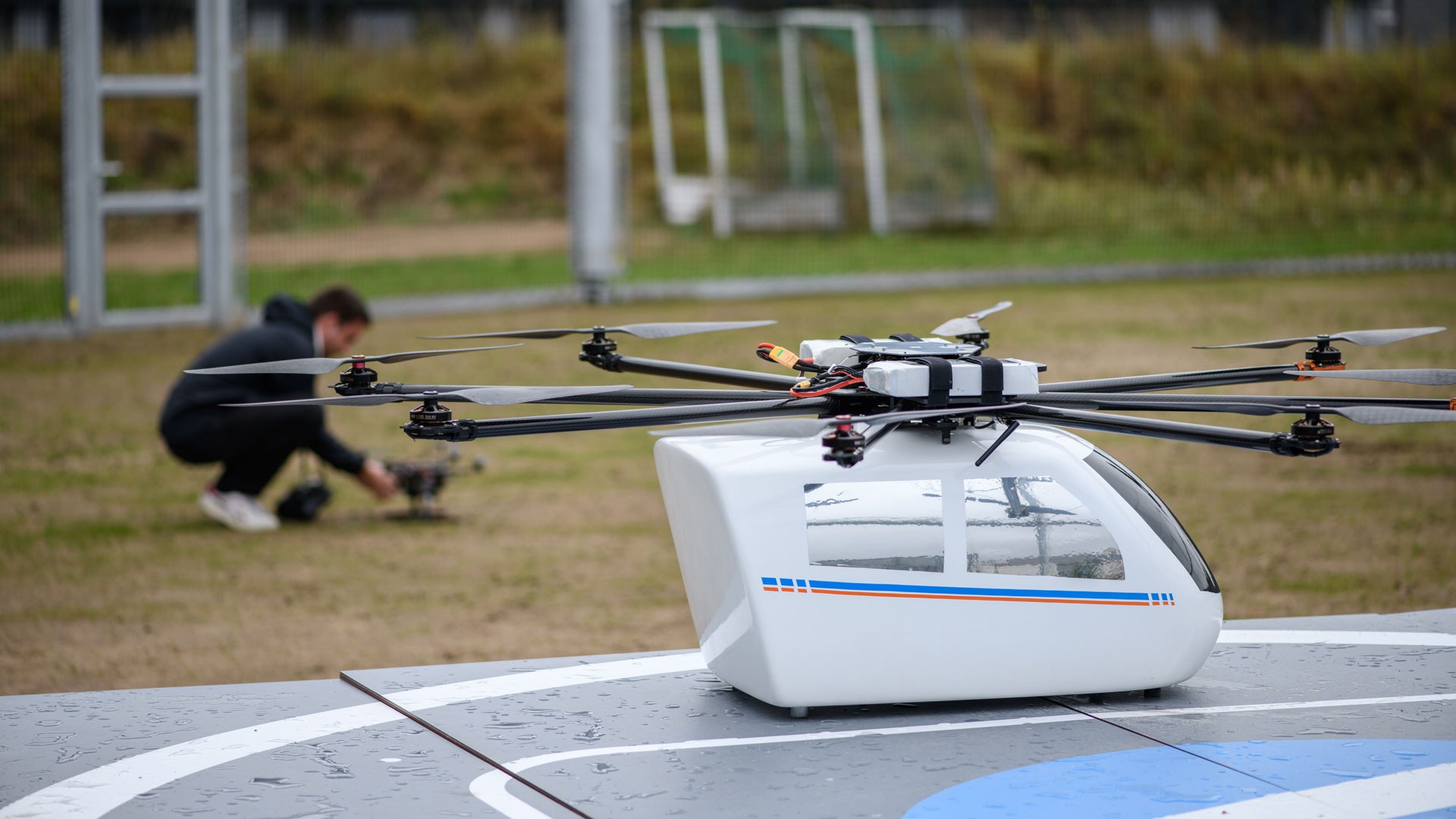 Das Bild zeigt einen Drohnen-Prototypen auf seiner Landeplattform. Im Hintergrund wird eine andere, kleinere Drohne für den Flug vorbereitet.