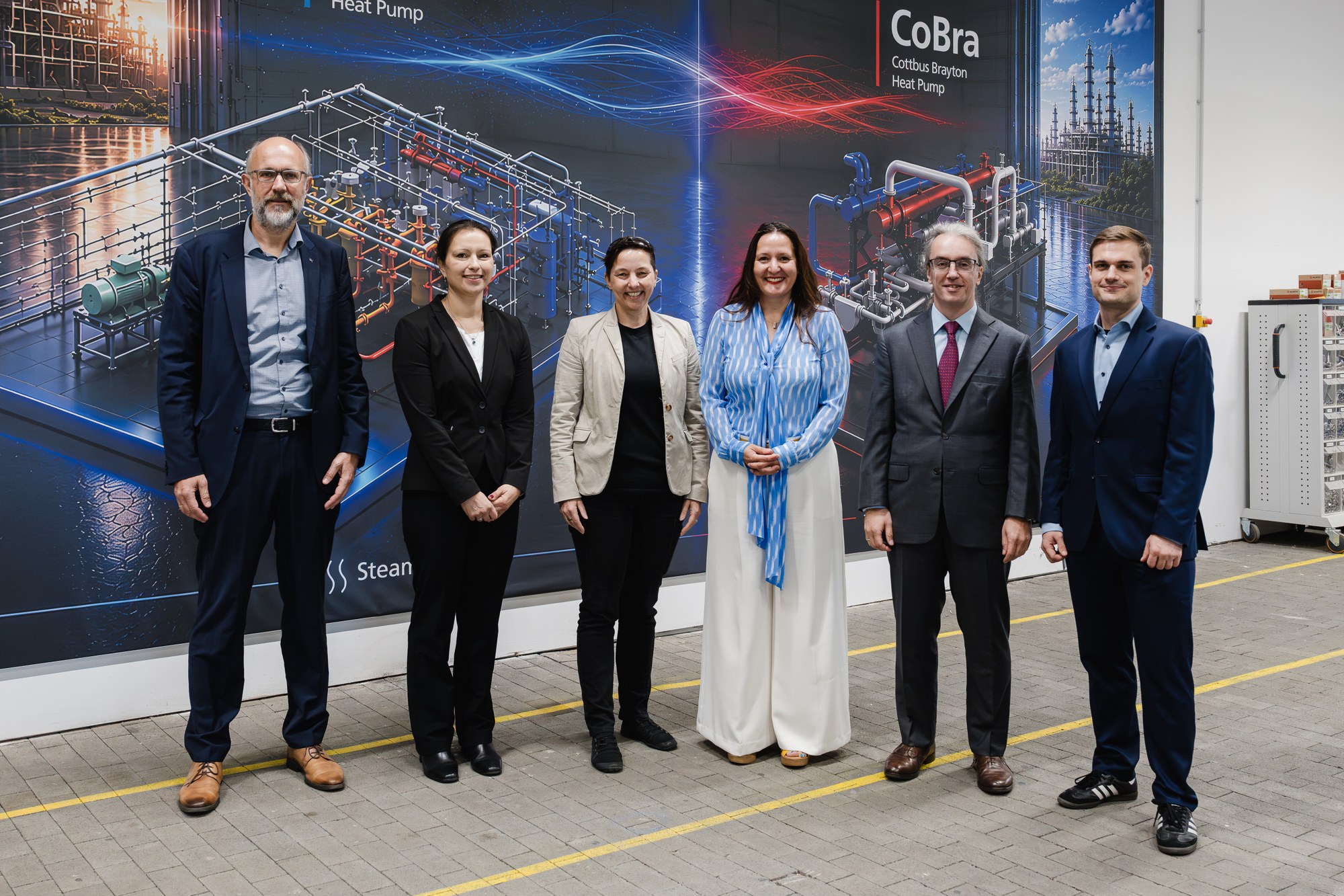 Gruppenfoto mit Dr. Manja Schüle vor einer Bildwand mit Wärmepumpen