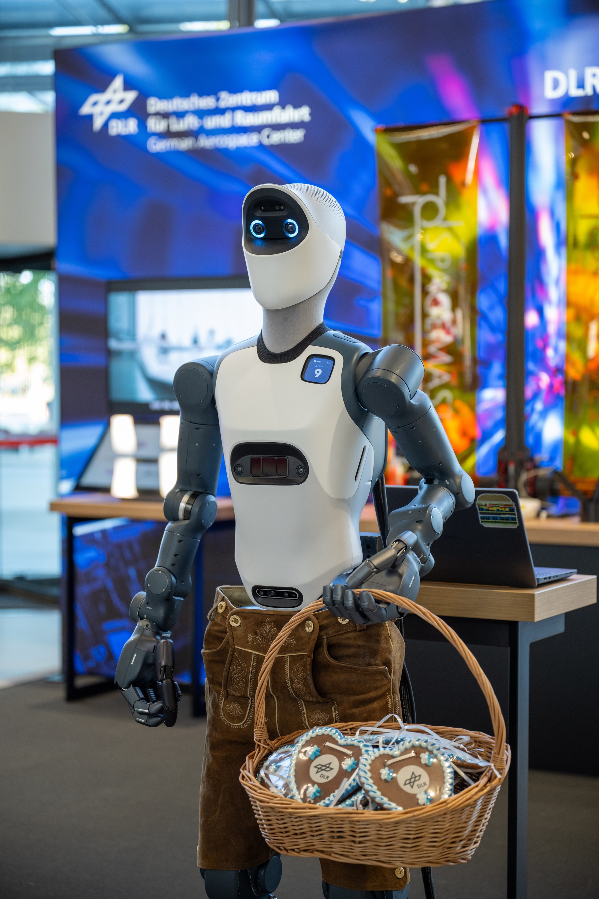 Humanoider Roboter bekleidet mit bayrischer Lederhose und einem Korb mit Lebkuchenherzen der Ausgründung Agile Robots am DLR-Stand der Bits & Pretzels.