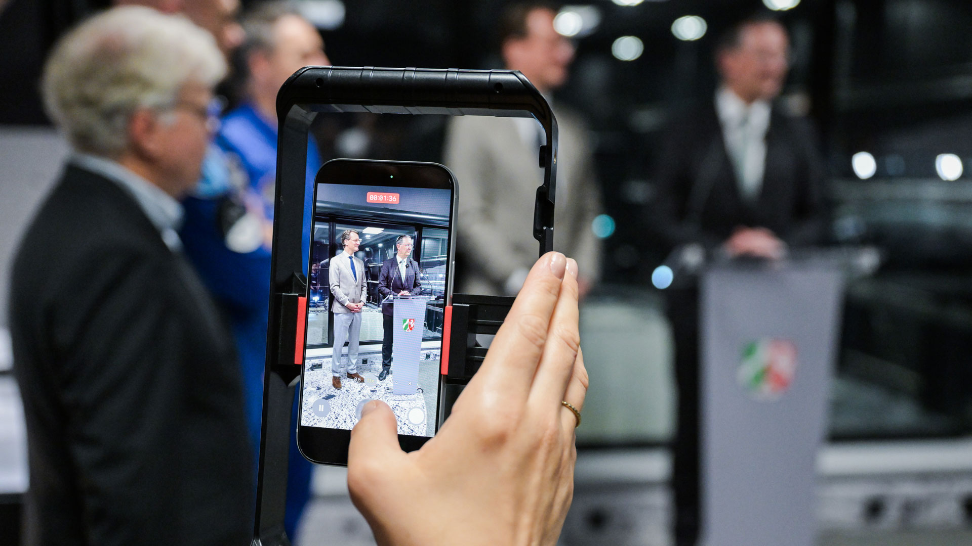 Auf einem Handy-Bildschirm sind zwei Personen im Besucherraum des Mondzentrums LUNA zu sehen: NRW-Ministerpräsident Hendrik Wüst und Stephane Beemelmans, stellvertretender Vorstandsvorsitzender des DLR.