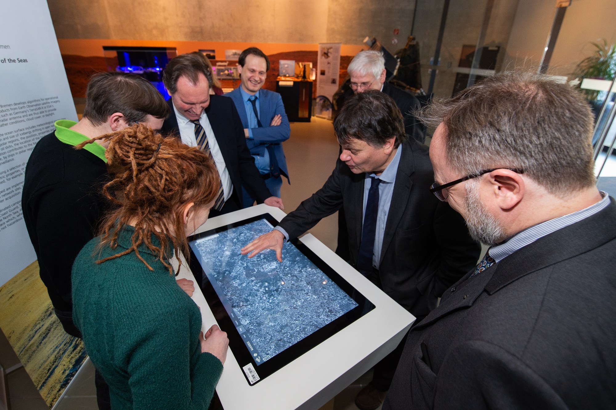 Aus Radaraufnahmen unterschiedlicher Satelliten können Informationen über den Zustand der Meere extrahiert werden, z. B. Wind, Seegang und treibende Eisberge. Senator Strehl bestaunt die Visualisierung auf dem Display.