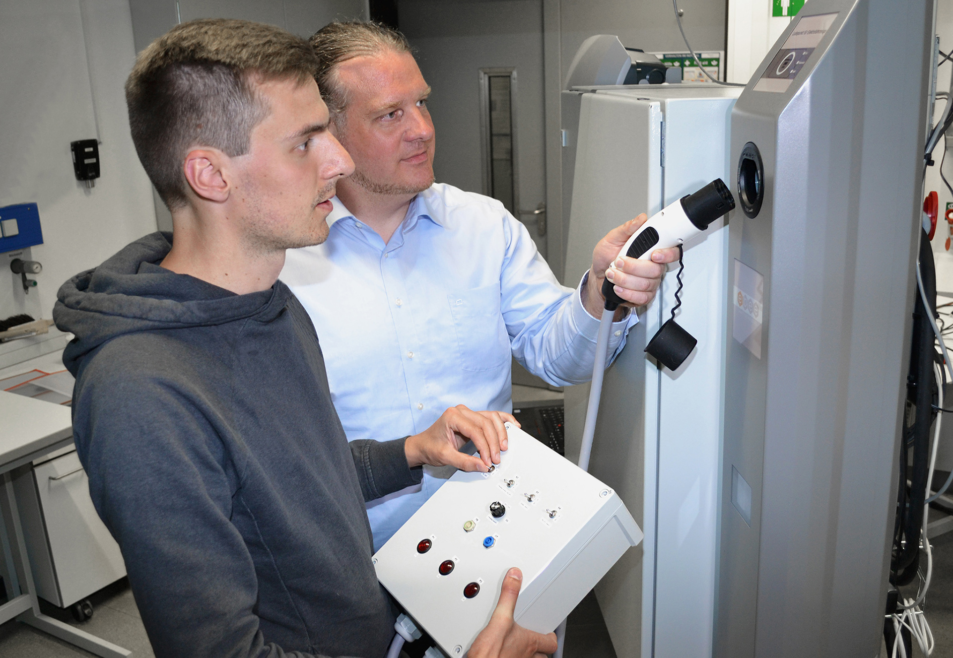 Projektleiter Jan-Simon Telle (links) und Projektmitarbeiter Dr. Benedikt Hanke an einer Ladesäule des EMGIMO-Teststands.