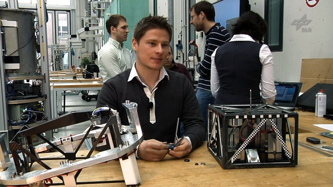 Testleiter Christian Grimm sitzt vor dem Asteroidenlander MASCOT am Tisch