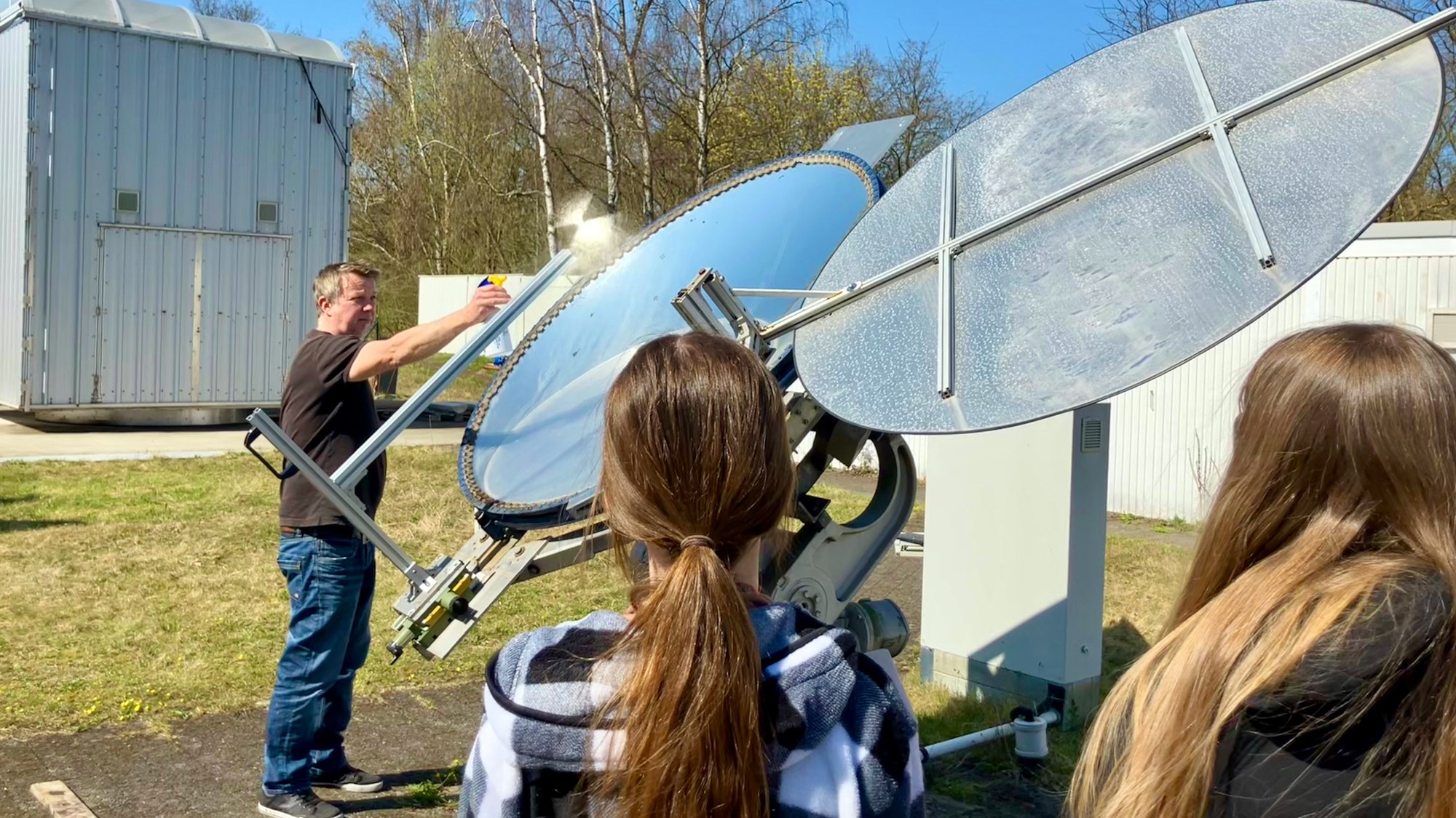 Ein Wissenschaftler steht vor einem Diskus-Spiegel und sprüht mit Wasser, so dass der Brennpunkt des Lichtes sichtbar wird.