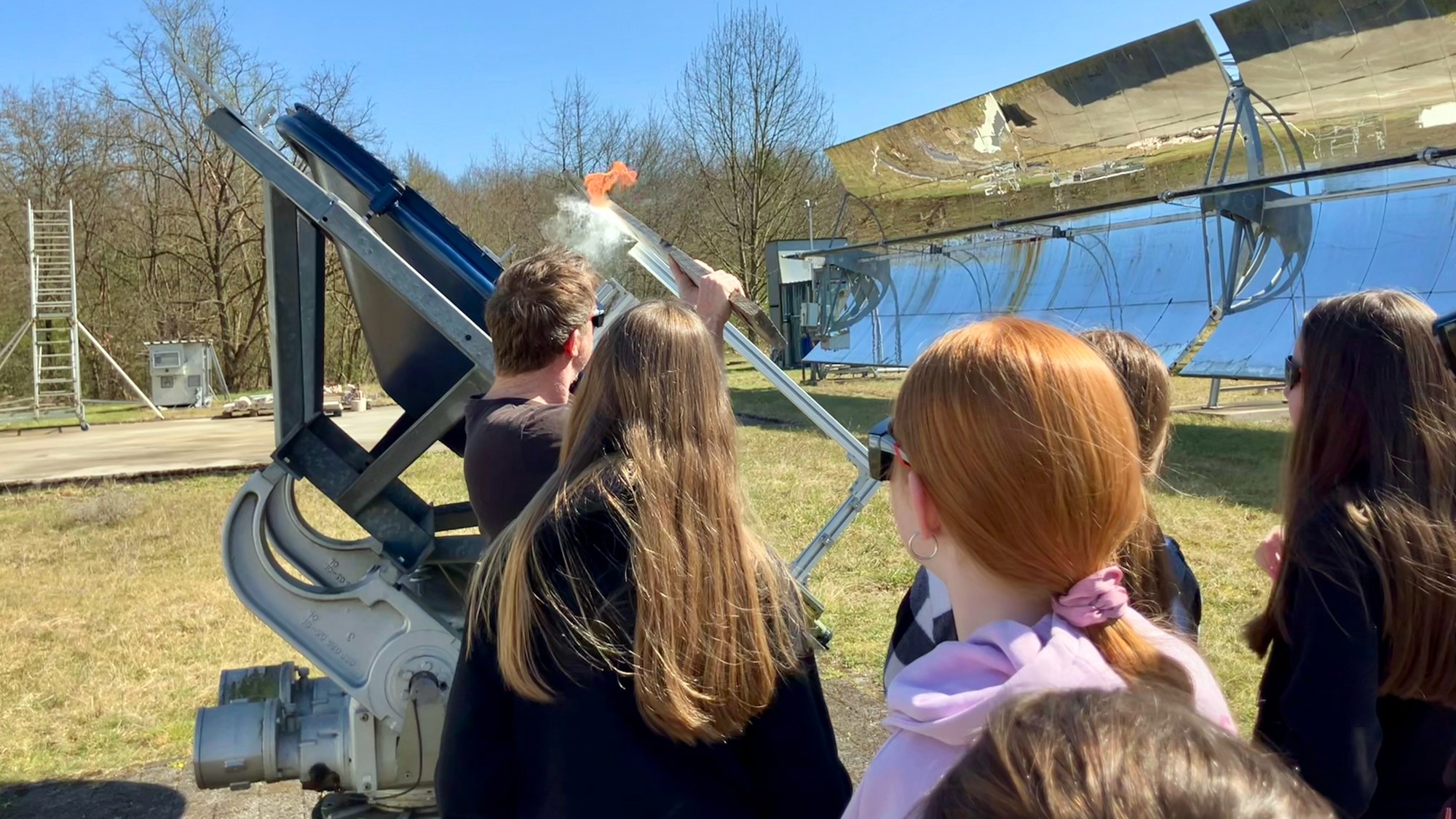Ein Wissenschaftler hält ein Stück Holz in den Brennpunkt, welches daraufhin Feuer fängt.