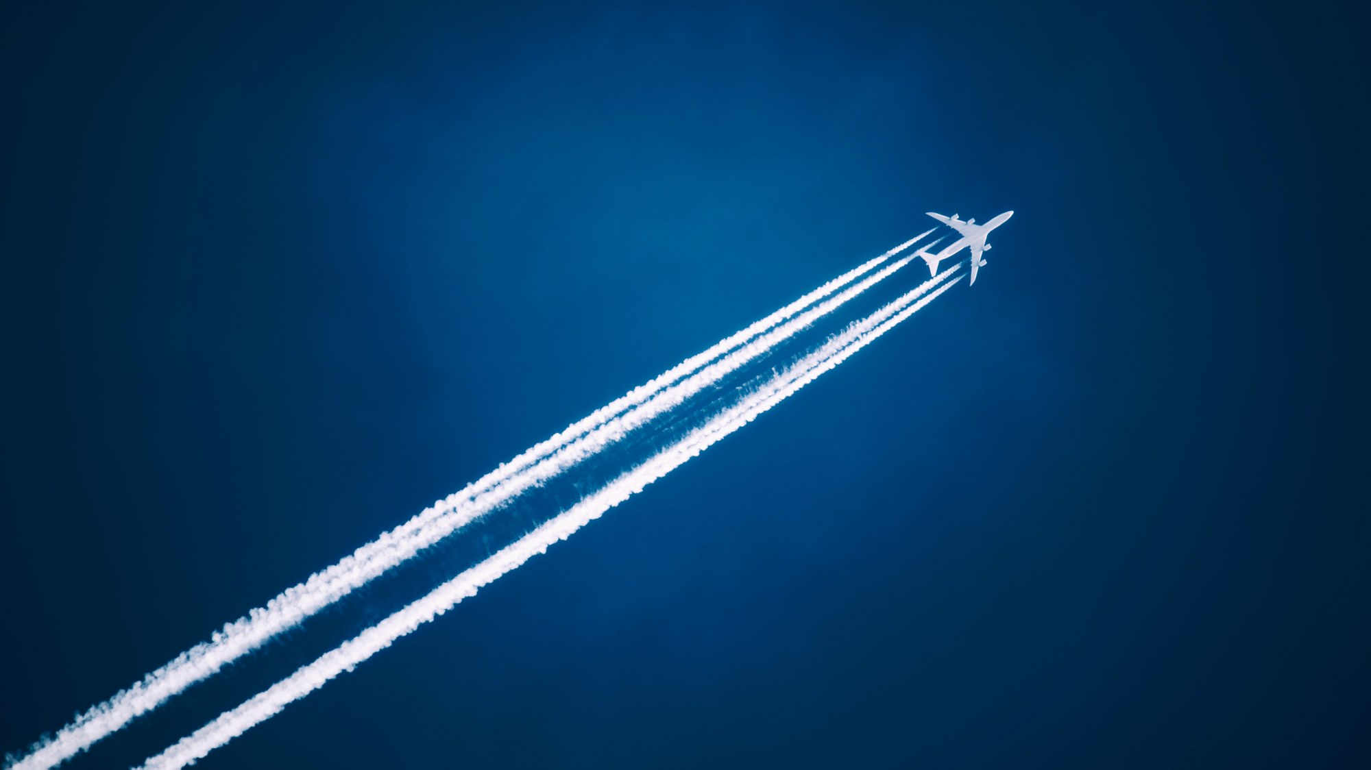 Ein Verkehrsflugzeug mit einem klaren Kondensstreifen über einem dunkelblauen Himmel (Symbolbild).