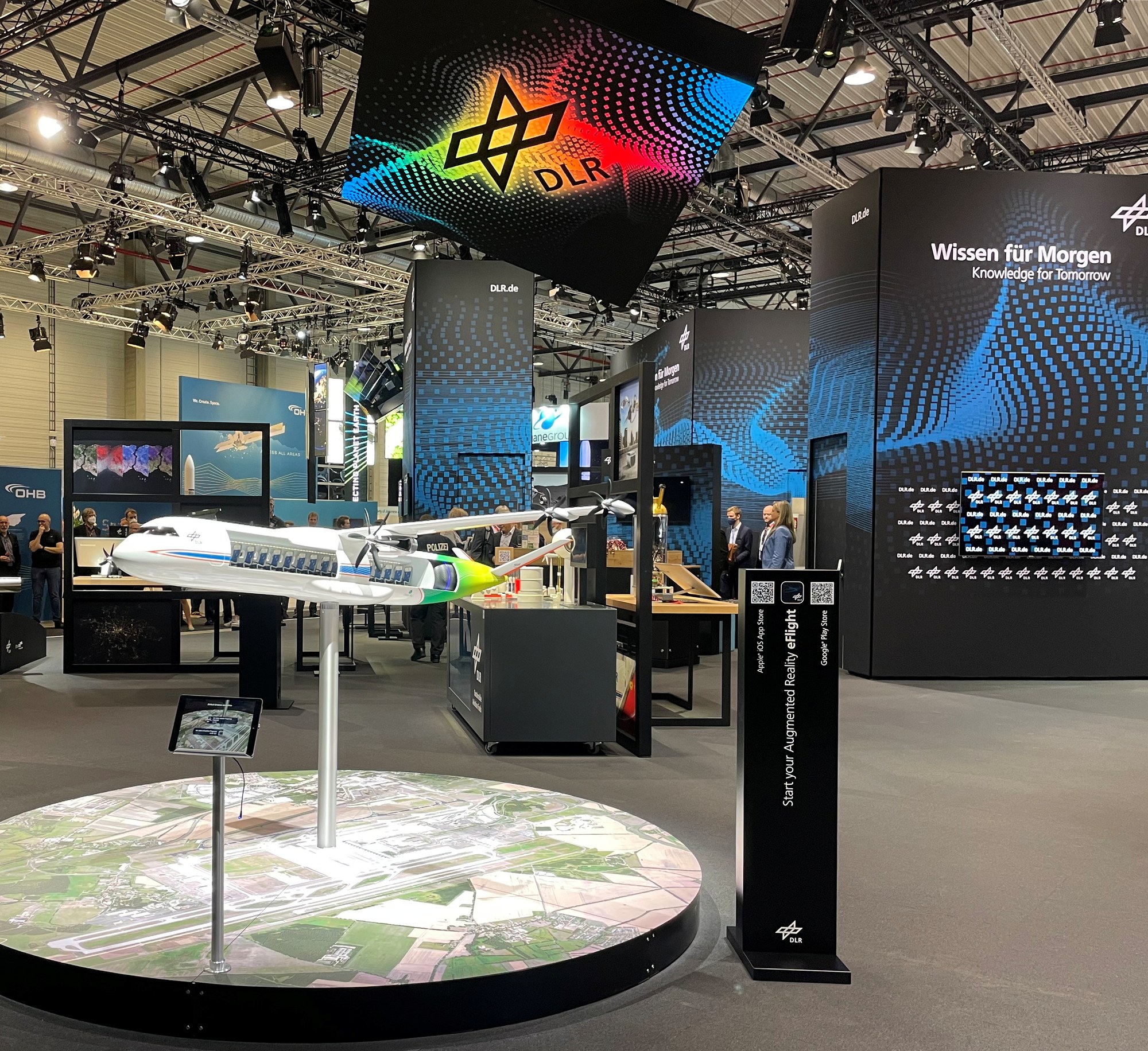 DLR-Messestand im Rahmen der ILA in Berlin. Verschiedene Exponate sind zu sehen, u.a. ein Flugzeugmodell.