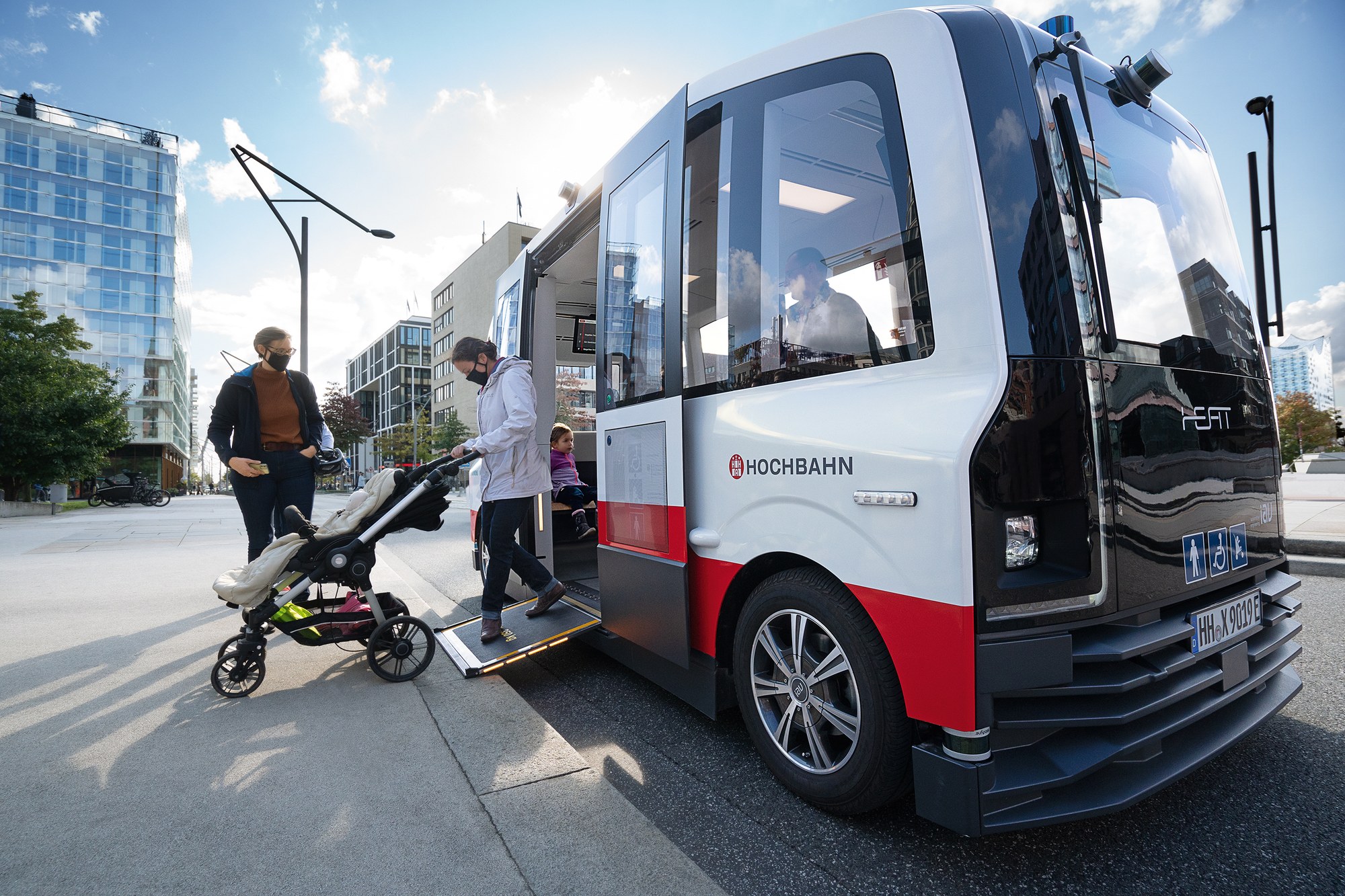 Zu sehen ist ein Fahrzeug mit zwei Personen und ein Kinderwagen beim Ausstieg oder Einstieg.