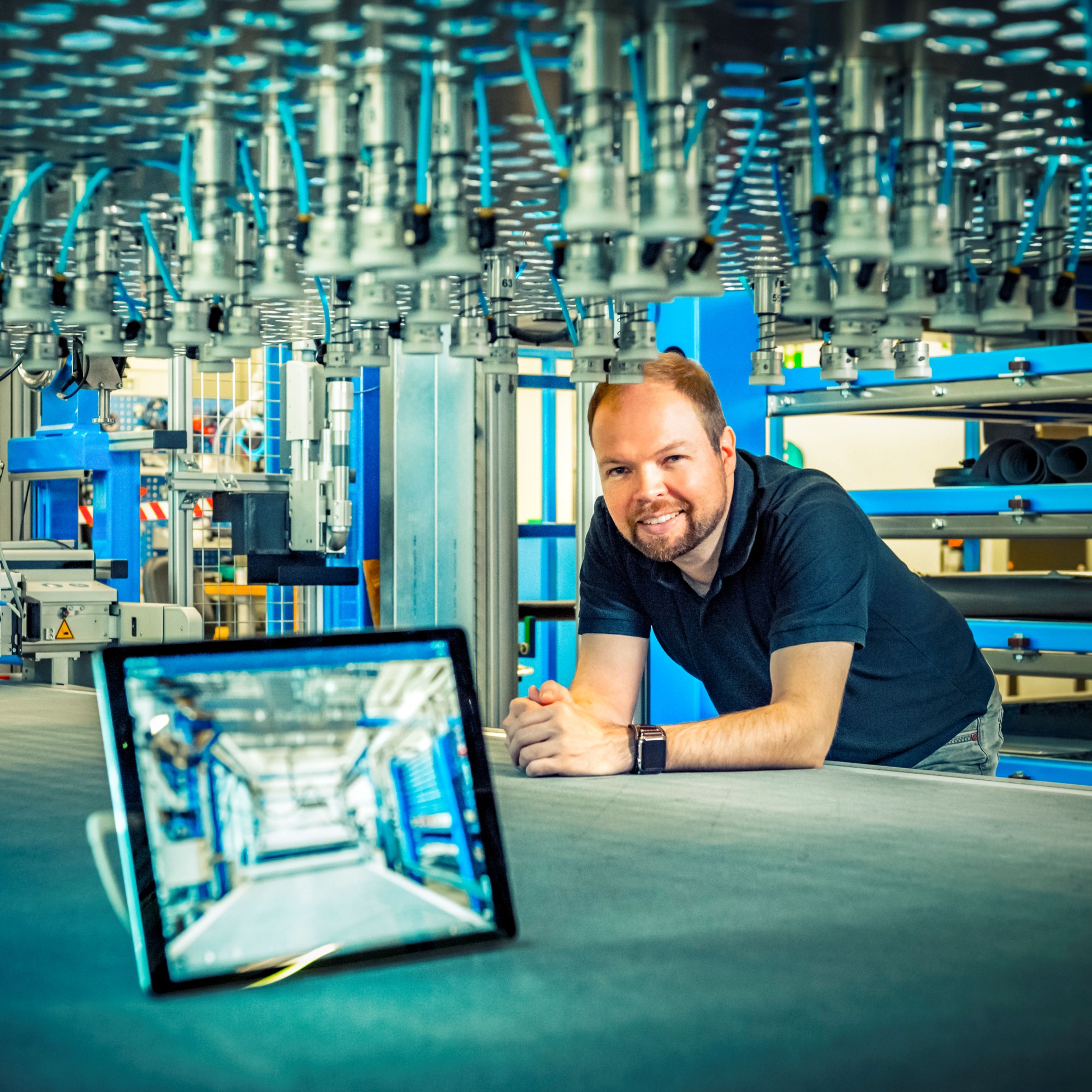 Ein Tablet im Vordergrund und ein Mitarbeiter in seinem Arbeitsumfeld.