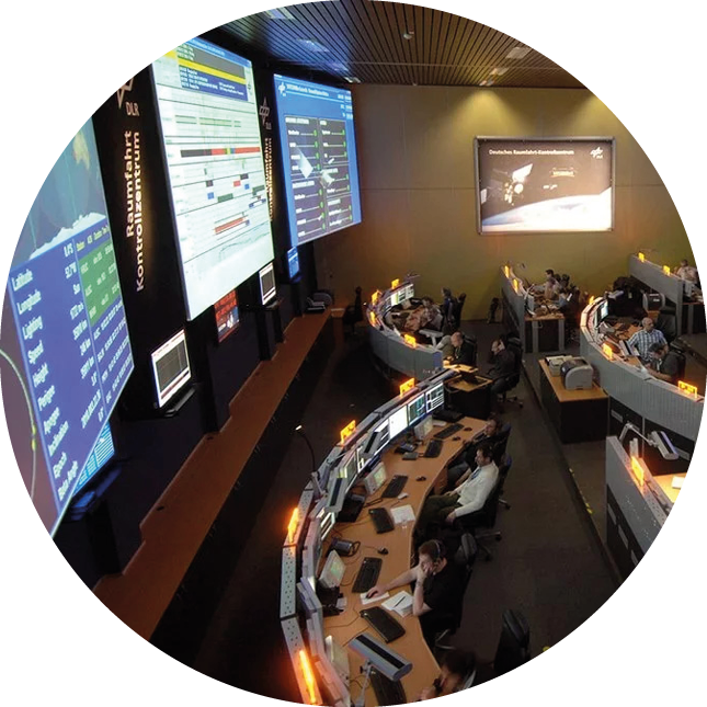 Das Bild zeigt einen Kontrollraum mit Bildschirmen.
