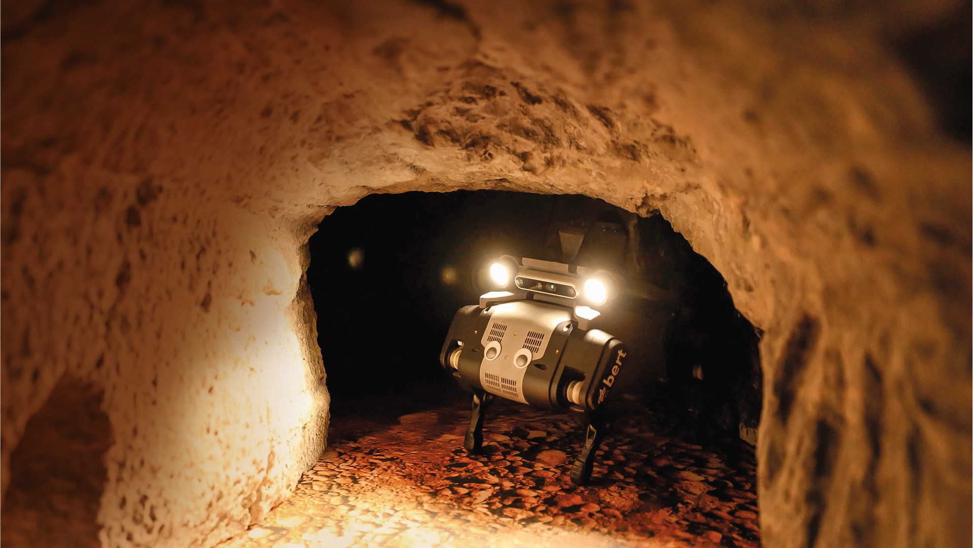 Ein kleiner Roboter in einer Höhle. Er beleuchtet seine Umgebung. Mittig sind Kulleraugen aufgeklebt.
