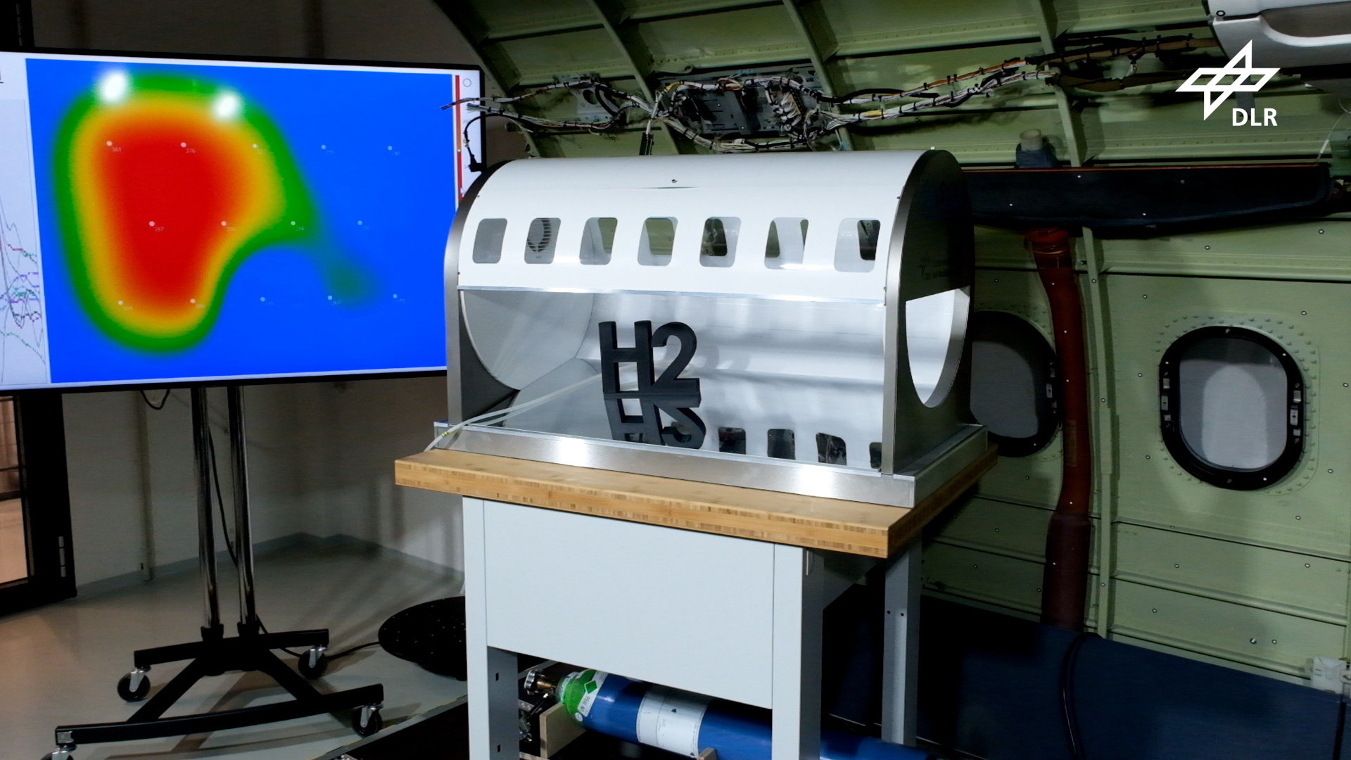 Zu sehen ist der Demonstrator in Form eines Flugzeugrumpf-Modells vor einem Monitor, der die gemessenen Gaslecks darstellt.