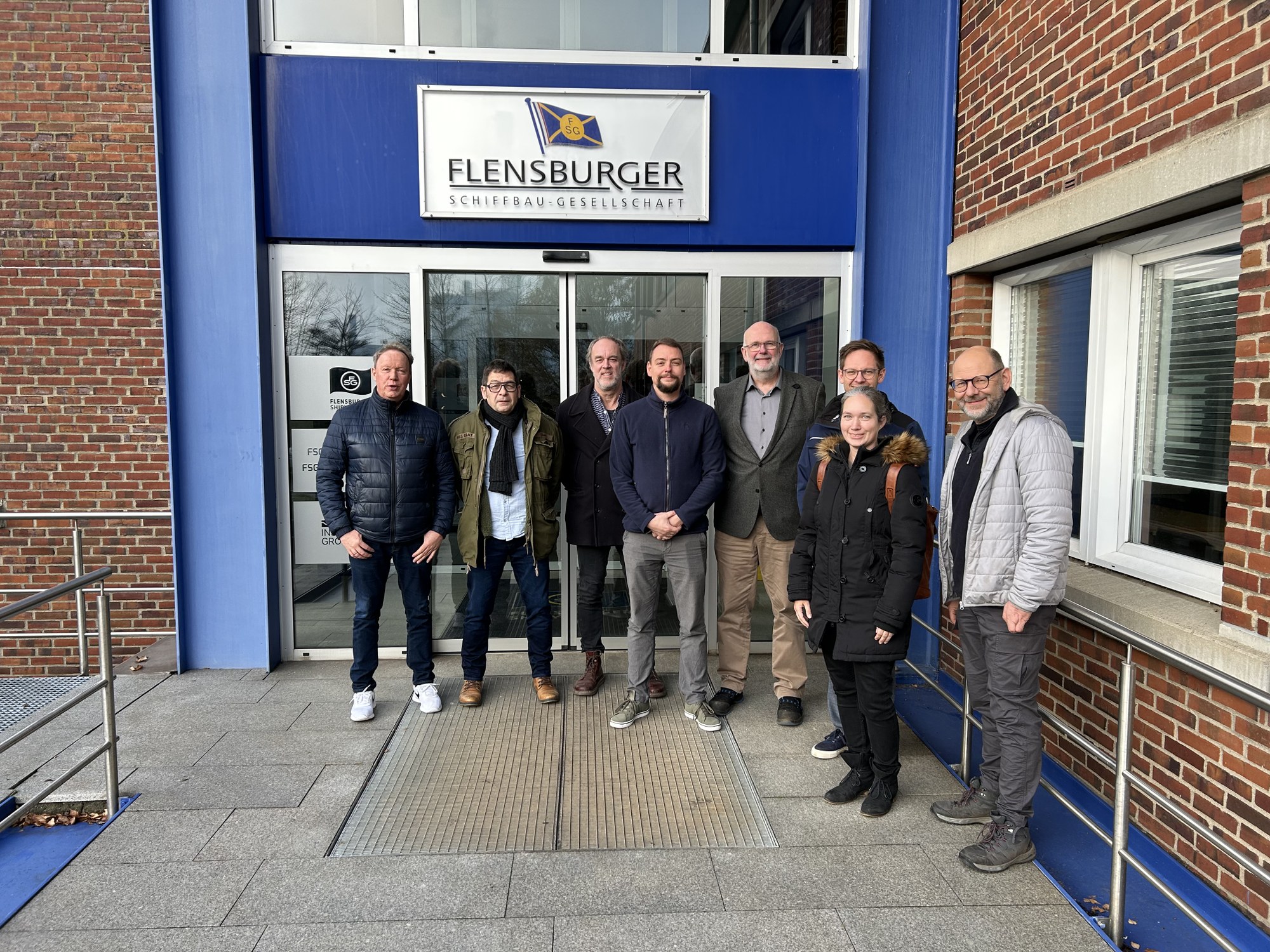 Eine Gruppe Personen stehen vor dem Eingang der Flensburger Schiffbau-Gesellschaft.