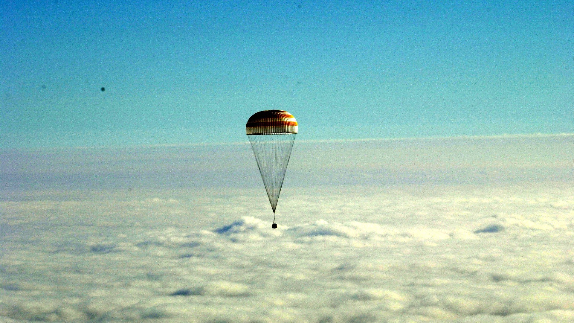 Eine Sojus-Landekapsel gleitet am Fallschirm zur Erde zurück.