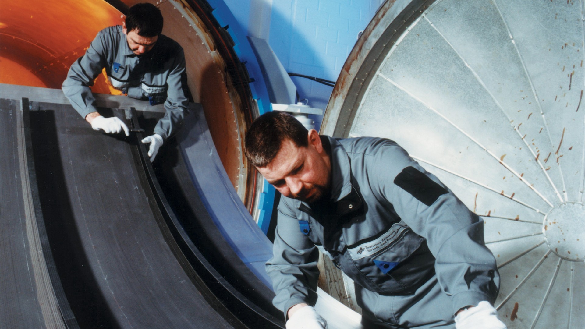 Zwei Männer verarbeiten eine Rumpfschale aus kohlefaserverstärktem Kunststoff