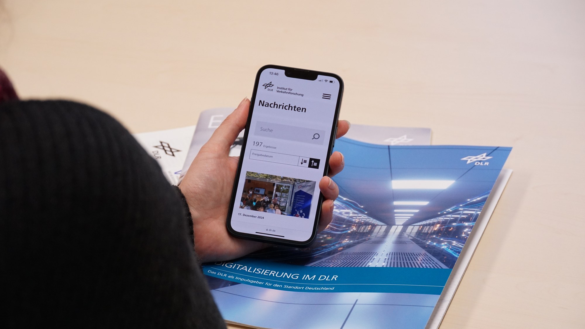 Zu sehen ist eine Person die ein Smartphone hält. Auf dem Smartphone ist die Nachrichtenseite des Instituts für Verkehrsforschung geöffnet.