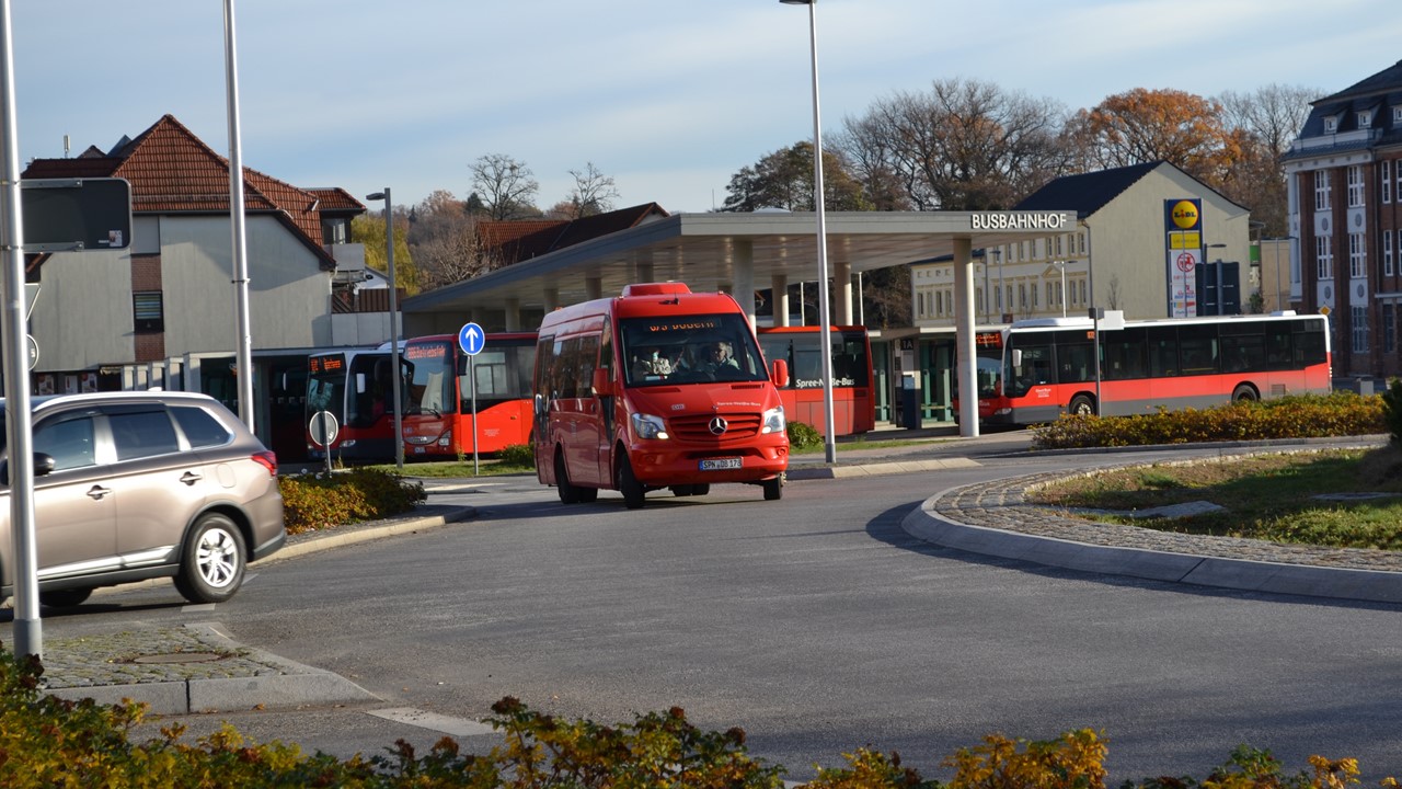 Ein roter Kleinbus fährt in einer Kurve auf die Betrachtenden zu.