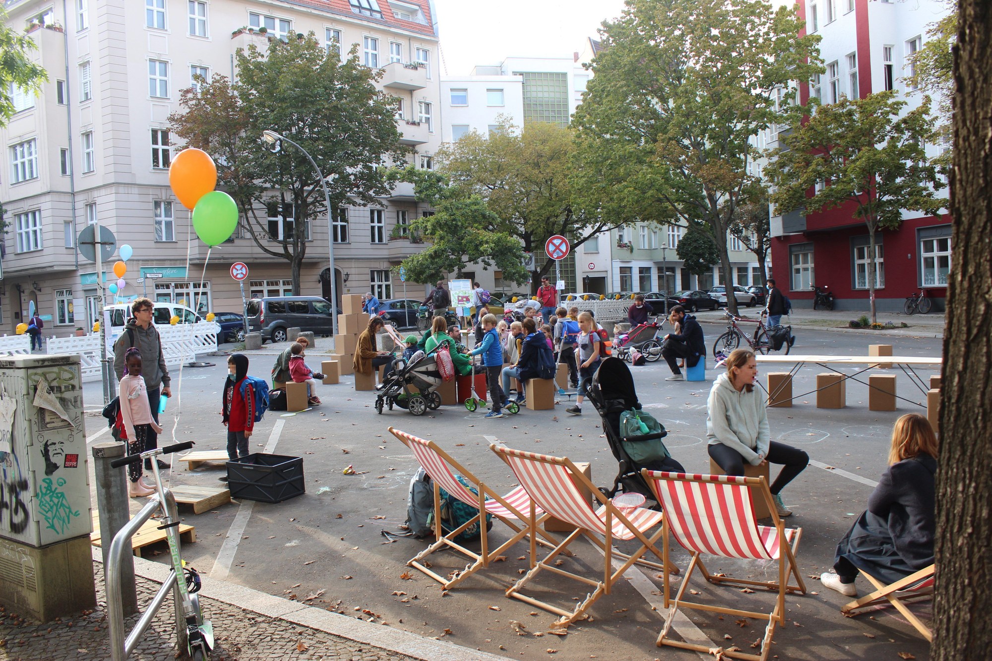 Ein öffentlicher Platz umfunktioniert - mit Strandstühlen, Luftballons und spielenden Kindern auf der Straße.