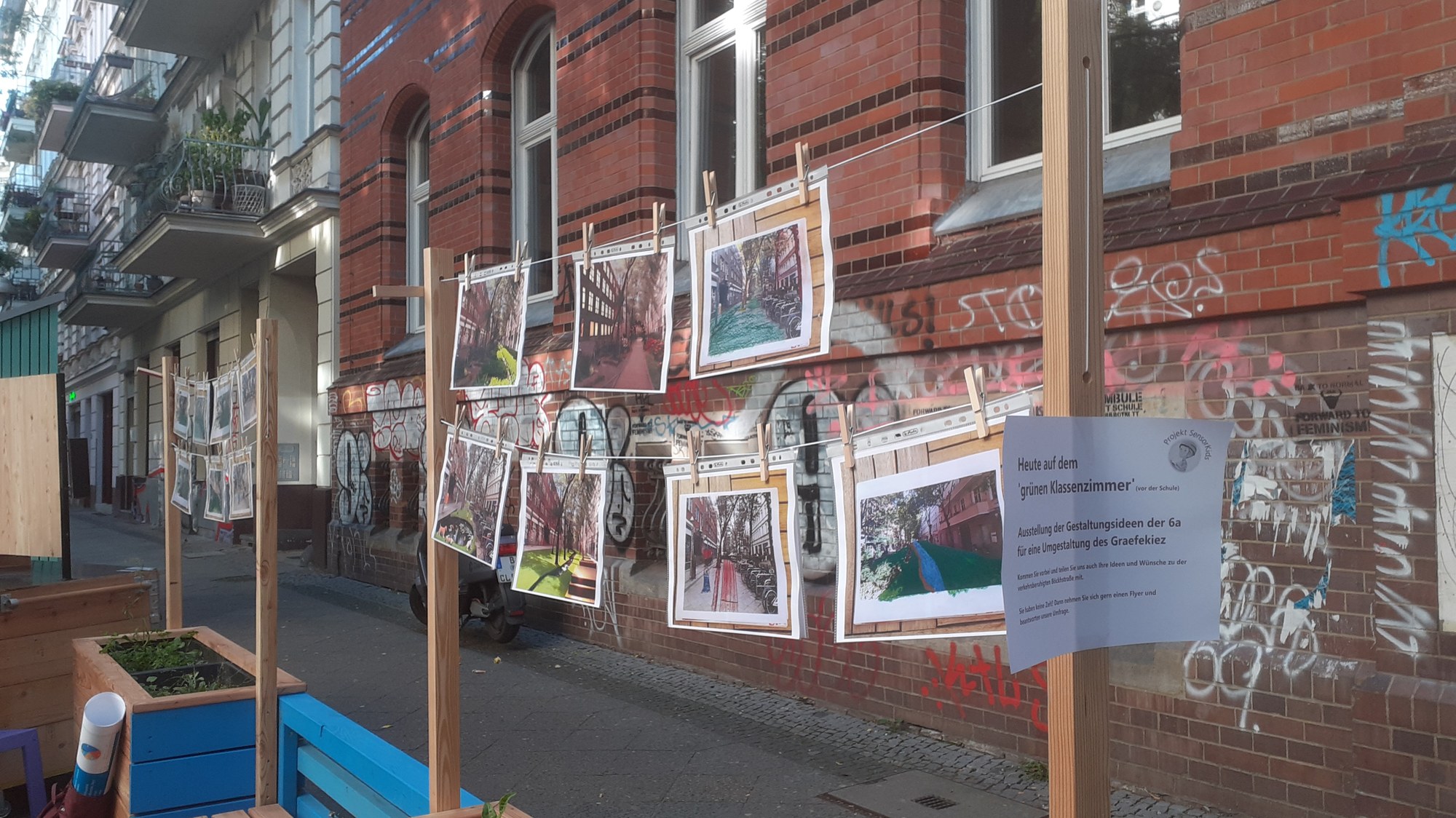 Mehrere Bilder hängen an einer Leine, davor ist ein Schild angebracht, dass es sich um eine Ausstellung der 6a zum Thema Umgestaltung handelt.