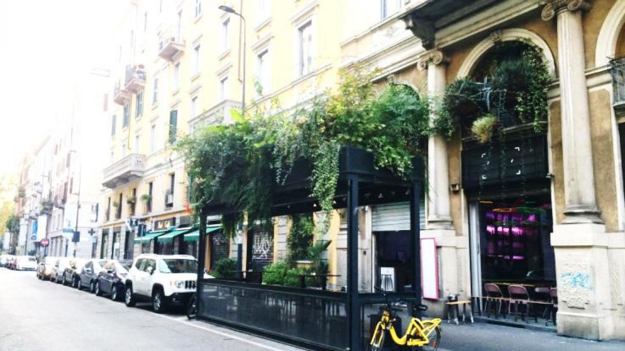 Zu sehen ist eine innerstädtische Straße. Es wurden Parkplätze gegen eines begrünten Aufenthaltsbereich ausgetauscht.