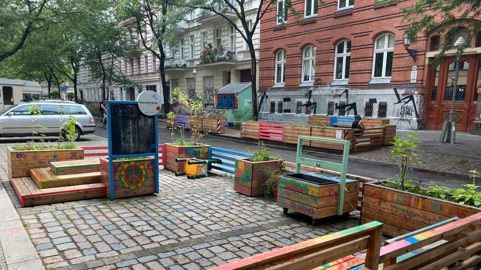 Ein Blick auf die Böckhstraße. Einige der Parkbuchten sind zu Kiezterrassen umgestaltet. In den Holzkonstruktionen sind bepflanzte Kübel, welche die Straße weiter begrünen.