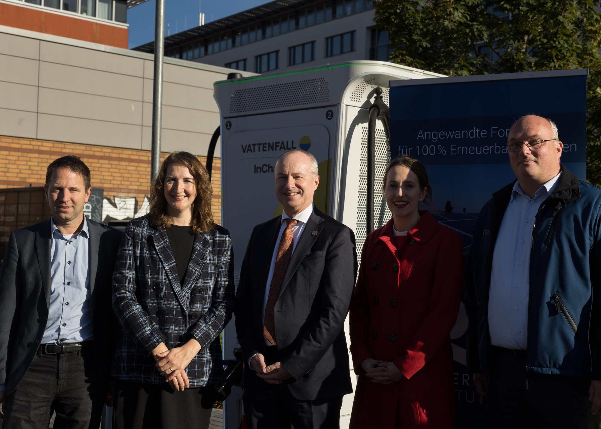 5 Personen stehen auf einem Supermarktparkplatz vor einer Ladesäule.