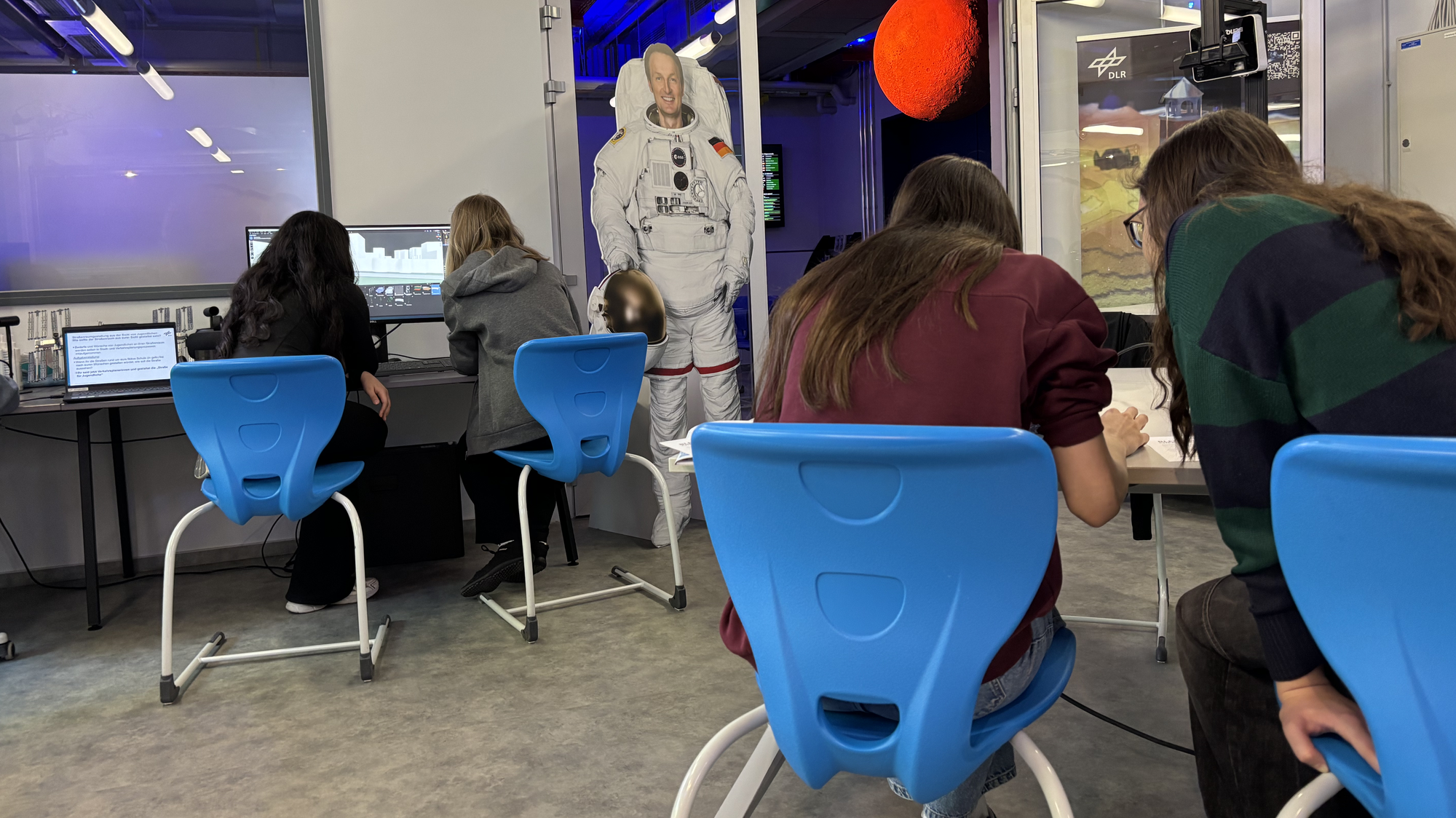 Girls' Day 2026: Schülerinnen sitzen an mehreren Tischen im DLR_School_Lab in Berlin-Adlershof. Konzentriert arbeiten sie jeweils zu zweit an Rechnern und nutzen die installierte 3D-Software, um ein Stadtviertel umzugestalten.