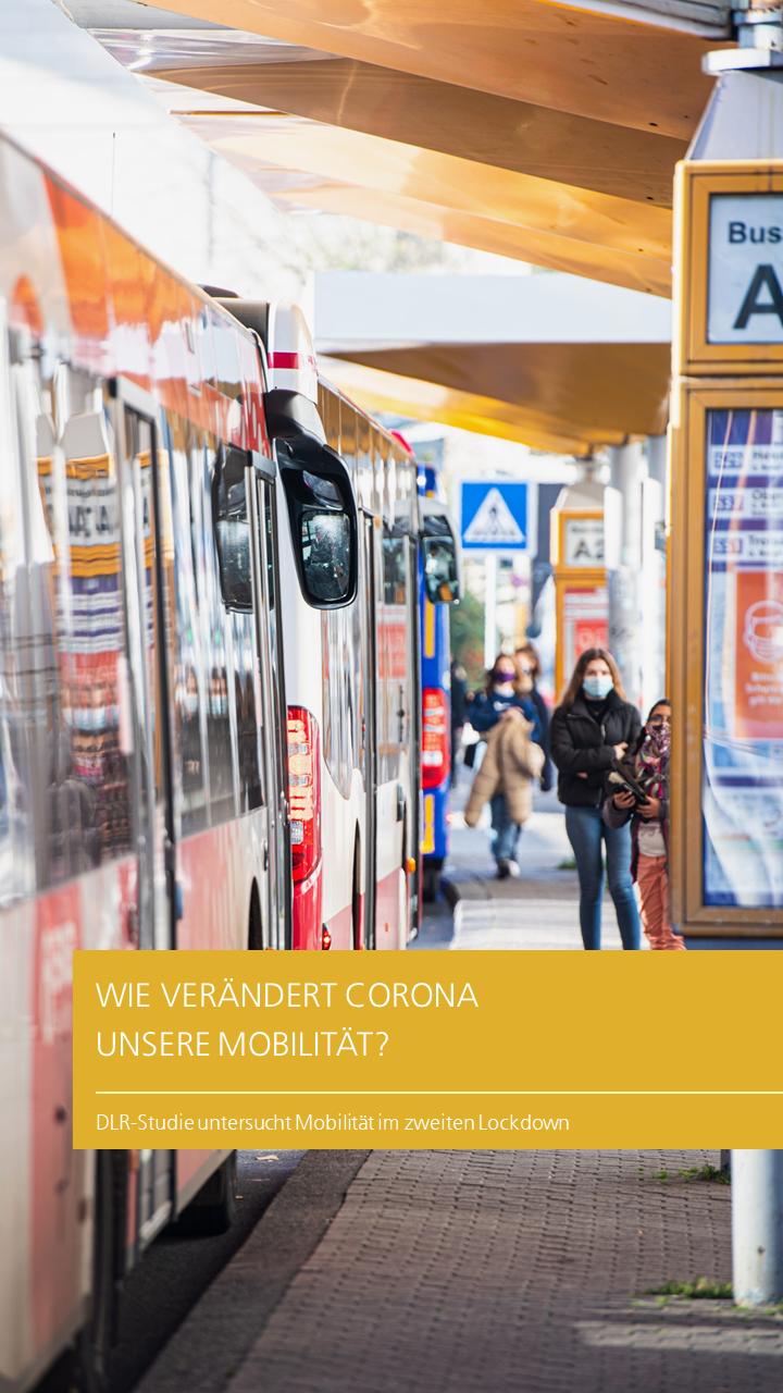Zu sehen ist ein Busbahnhof. Mehrere Busse befinden sich innerhalb diesem. Zwei weiblich gelesene Personen warten auf einen Bus. Sie tragen Gesichtsmasken.
