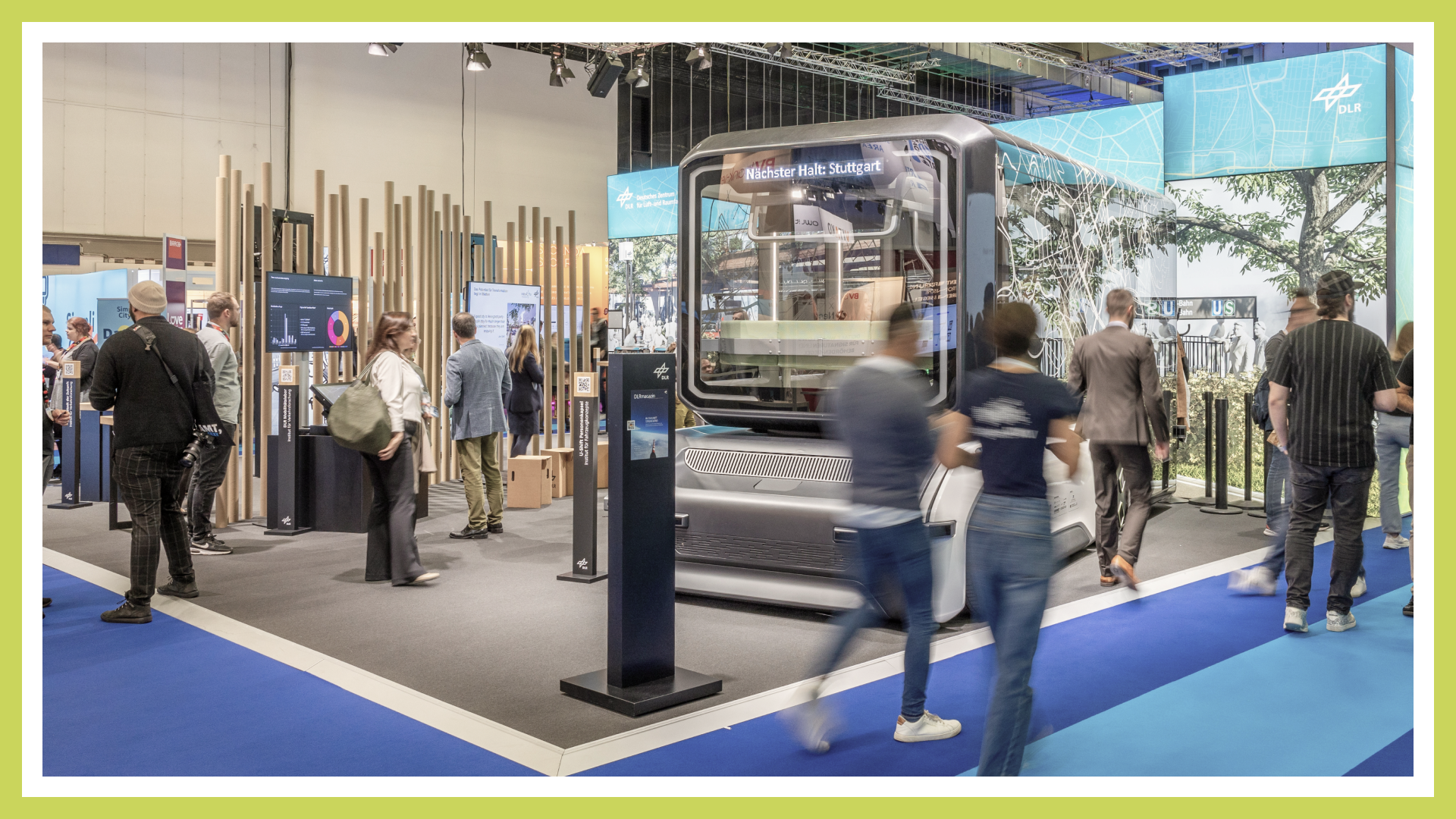 Zu sehen ist ein Veranstaltungsfoto des Messestands des Deutschen Zentrum für Luft- und Raumfahrt auf der Smart Country Convention 2024. Es ist das Exponat "U-Shift" im Vordergrund zu sehen sowie mehrere Menschen.