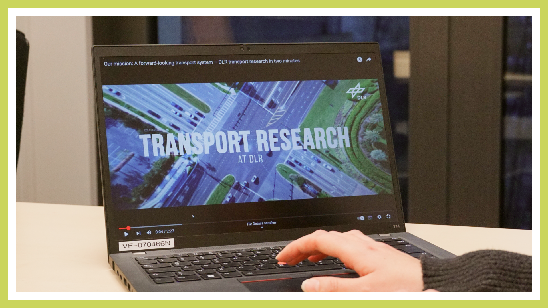 Ein geöffneter Laptop spielt das Video „Transport Research at DLR“ ab. Eine Hand ist zu sehen, während die Person den Laptop bedient.