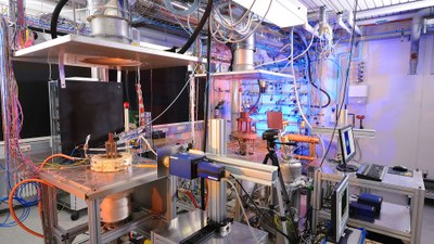 Das Bild zeigt zwei unterschiedlich große atmosphärische Verbrennungsprüfstände in einer Laborumgebung. Vorne im Bild ist eine OH*-Chemilumineszenz- Kamera aufgebaut.