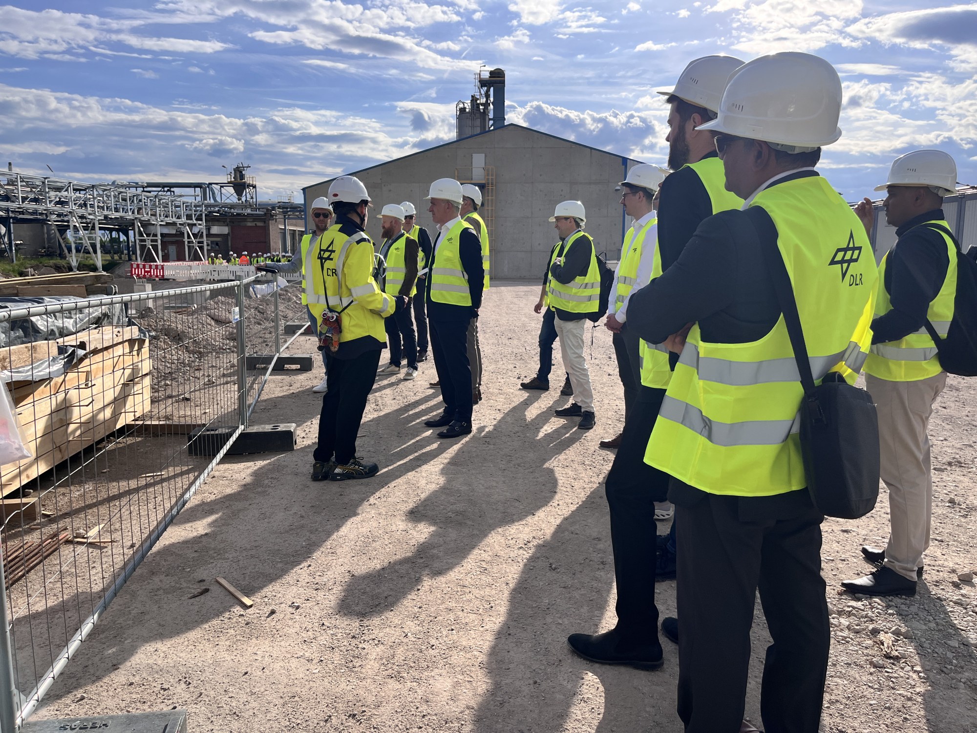 Mehrere Personen mit Helmen und Warnwesten stehen auf der Baustelle und lassen sich den Stand der Dinge bei den Bauarbeiten erklären.