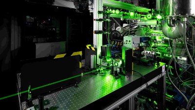 Das Bild zeigt den Hochdrückbrennkammerprüfstand HiPOT. Hinten rechts ist die optisch zugängliche Brennkammer zu sehen, in der Bildmitte ein komplexes optisches System für die eingesetzte Lasermesstechnik.