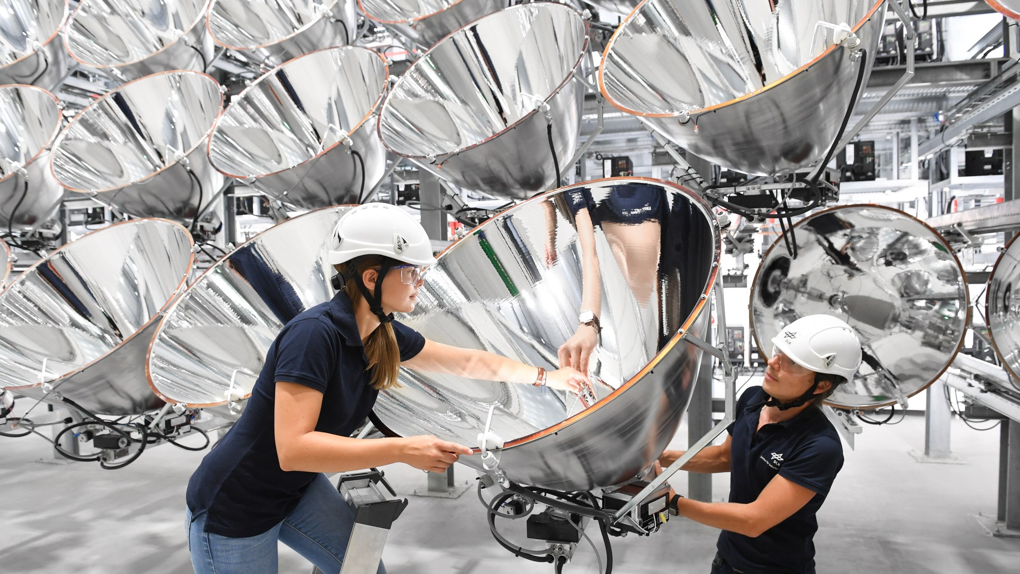 Two DLR researchers change a light source on one of the 149 high-power radiators of the Synlight.