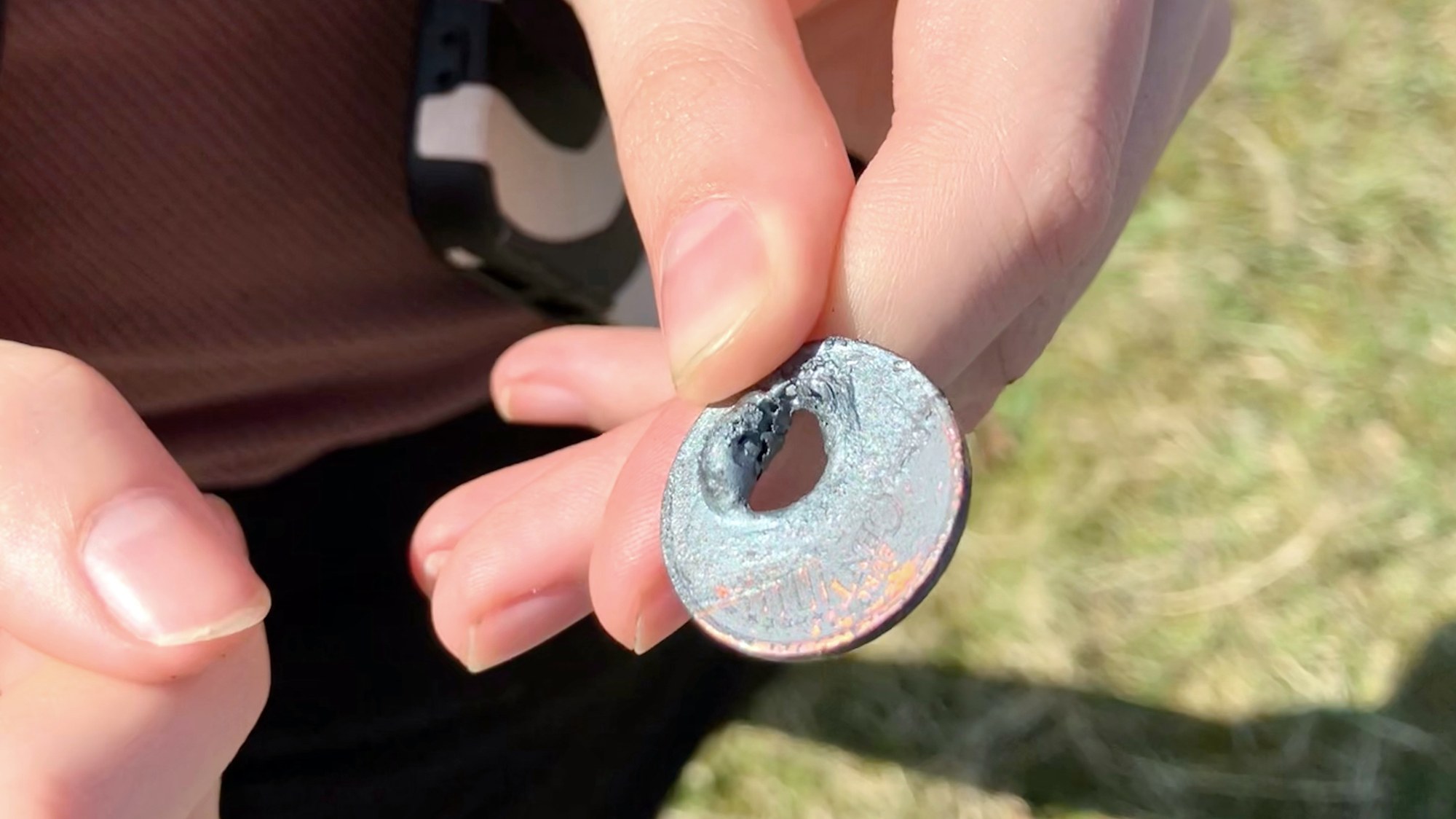 A schoolgirl is holding a 5 cent coin with a hole between her fingers.