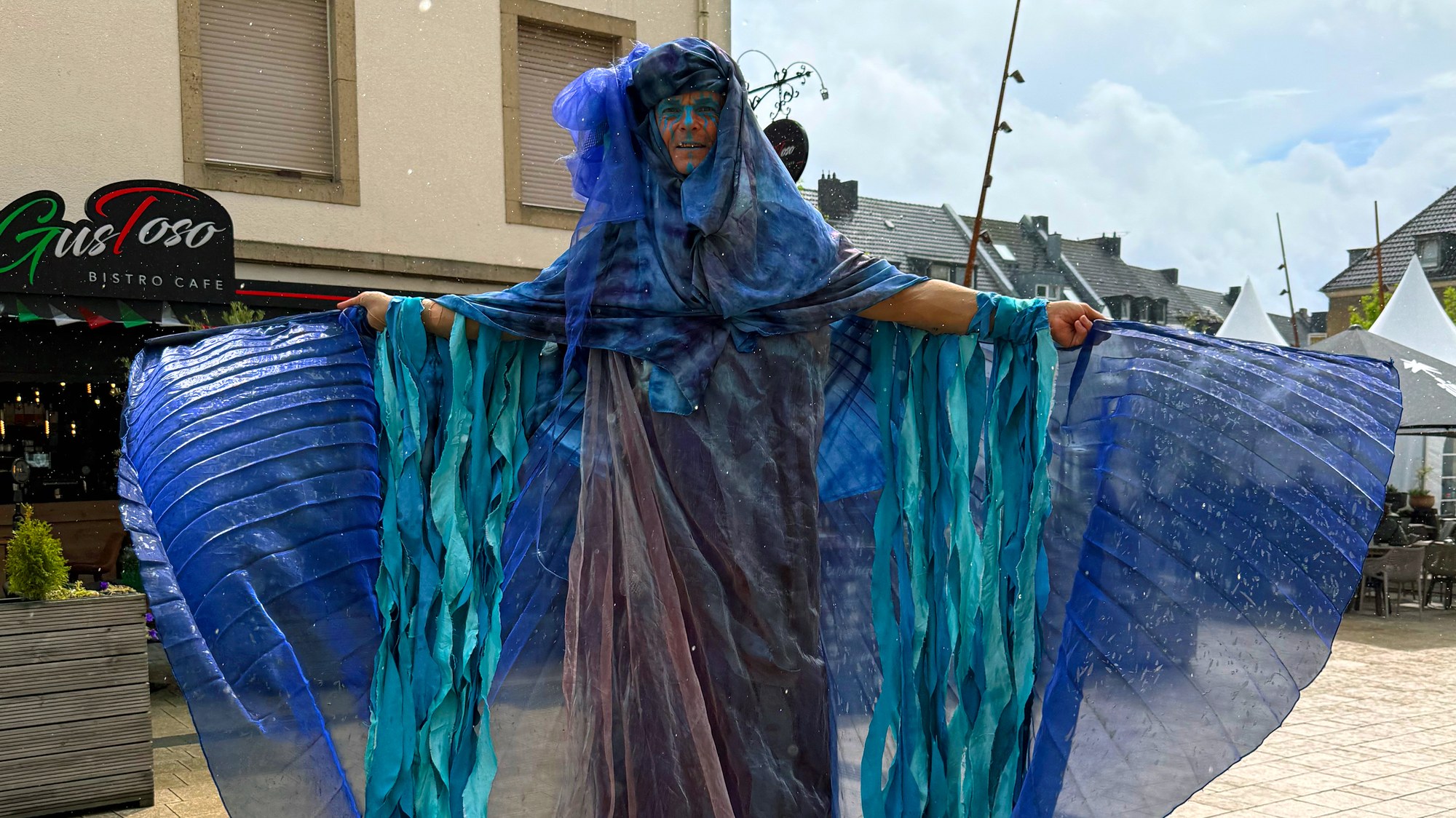 A disguise artist in a blue butterfly outfit on stilts