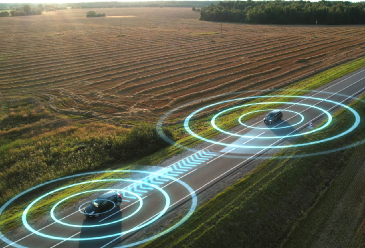 Illustrative image for EM 4.0 StartUp: connected smart cars on a country road. Interconnectivity is represented by concentric, glowing circles emanating from both cars.