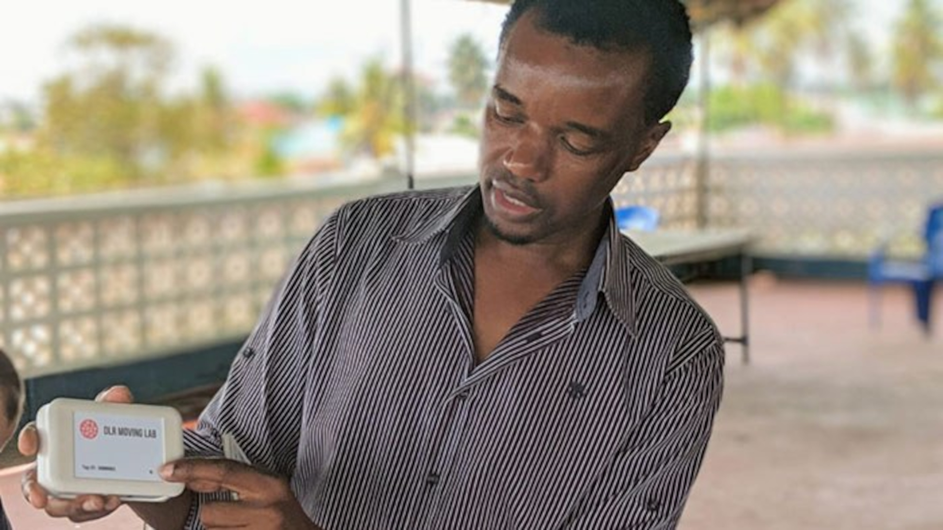 A Tanzanian holds a GPS logger from the DLR Moving Lab in his hand and looks at it while explaining something.