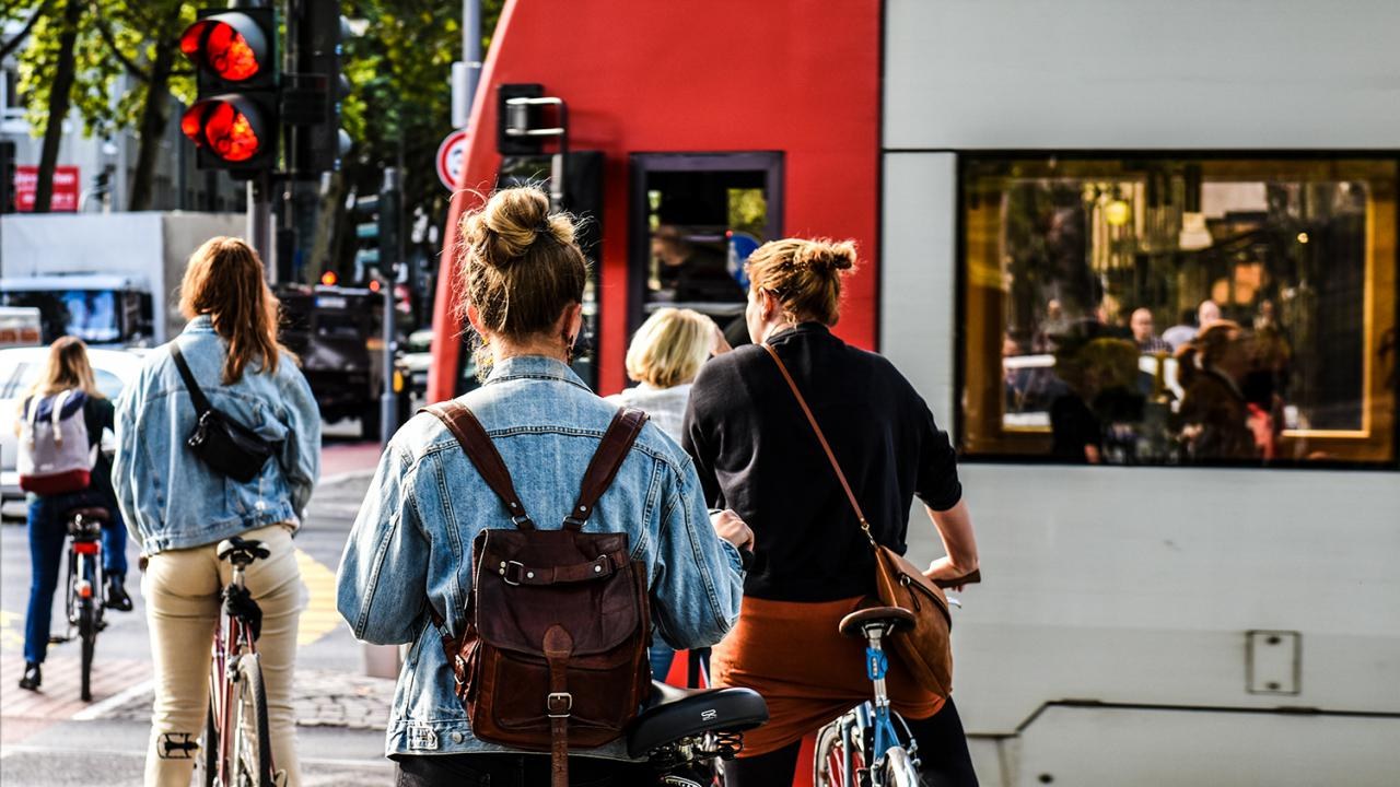 You can see a tram crossing a road. Cyclists are waiting for the tram to pass.