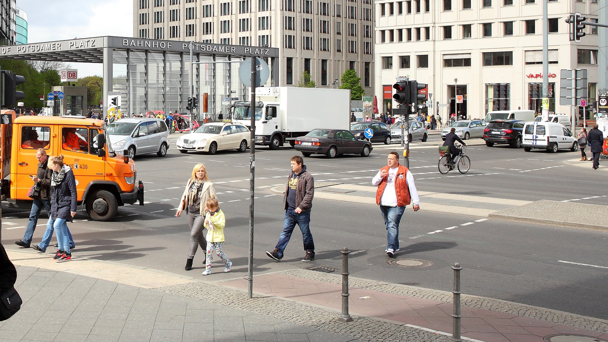 Several pedestrians cross at a traffic light on Potsdamer Platz in Berlin. On the left of the picture is a small lorry belonging to the Berlin municipal cleaning service. In the background, cars and lorries drive along Potsdamer Platz.