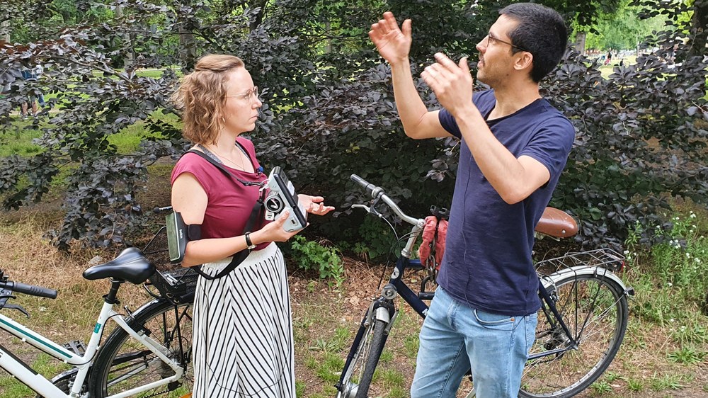 Two people are standing on a green field with their bicycles and looking at a map.