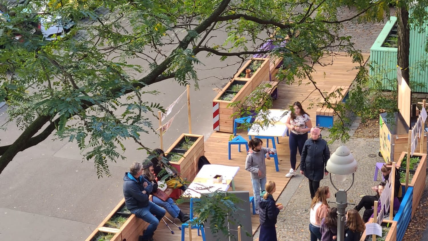 A section of road from above, several car parks have been replaced by self-built furniture and planters. some people use them.