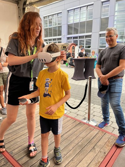 A woman puts VR glasses on a child. The father watches intently in the background.
